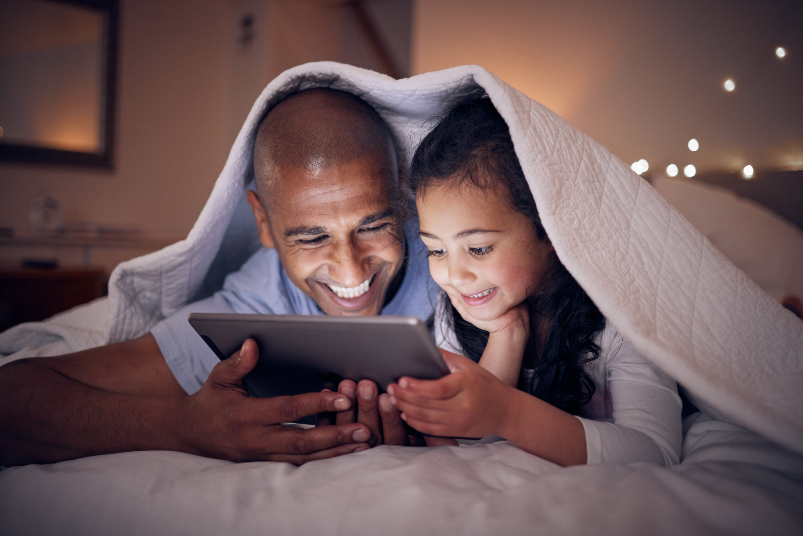 Father, kid and smile with tablet at night under blanket of online games, reading ebook or storytelling app. Happy dad, girl child or watch cartoon movie on digital tech, media or internet in bedroom.